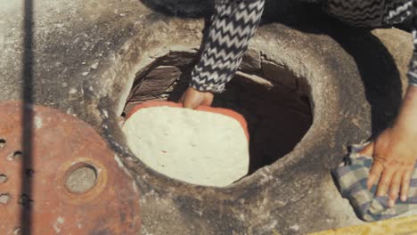 Refugee-woman-Afghan-places-dough-into-self-built-Tandoor-oven-in-Moria-refugee-camp