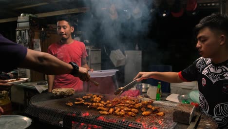 Vista-De-3-Hombres-De-Malasia-Asando-Sabrosas-Alitas-De-Pollo-En-Una-Parrilla-De-Barbacoa-Por-La-Noche