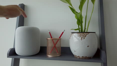 Tiro-Estático-En-Cámara-Lenta-Del-Hombre-Tocando-Dos-Veces-Con-Pausa-Un-Homepod-De-Apple-En-La-Parte-Superior-De-La-Estantería-De-Aspecto-Moderno-Adyacente-A-Un-Portalápices---Planta