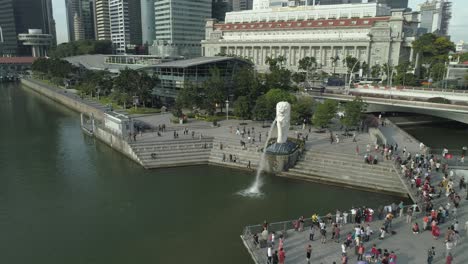 Volando-Alrededor-De-La-Famosa-Estatua-De-Merlion,-Símbolo-De-Singapur,-Rodeada-Por-Una-Multitud-De-Turistas-Que-Viajan-En-El-Centro-De-La-Ciudad-De-La-Metrópolis