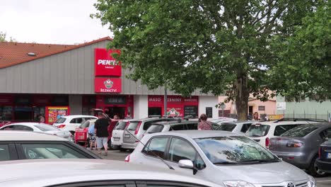 Gente-Caminando-Y-Autos-Estacionándose-Frente-A-Un-Supermercado-Penny-Market-En-Un-Agradable-Día-De-Verano