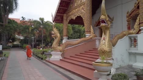 Langsamer-Schwenk,-Um-Den-Beeindruckenden,-Goldgerahmten-Eingang-Des-Wat-Phra-Singh-Tempels-Zu-Enthüllen,-Darunter-Zwei-Unglaublich-Detaillierte-Mythische-Drachenstatuen-Und-Ein-Junger-Mönch,-Der-Die-Treppe-Hinuntergeht