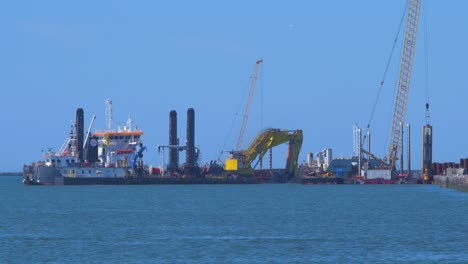 Barco-De-Dragado-De-Tolva-Trabajando-En-El-Puerto-De-Liepaja,-Grúa-Con-Cubo-Levanta-El-Suelo-De-La-Bahía,-Plano-Medio-Desde-La-Distancia