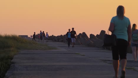 People-walking-on-the-Karosta-Northern-Pier-at-romantic-red-glowing-sunset,-medium-shot-from-a-distance