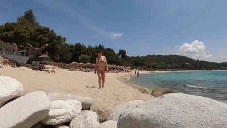 Young-girl-in-a-swimwear,-walking-on-a-sandy-beach-towards-the-camera