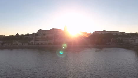 Toma-Estática-De-Un-Dron-Sobre-El-Río-Danubio,-El-Sol-Brilla-Desde-Detrás-Del-Lado-Del-Castillo-De-Buda