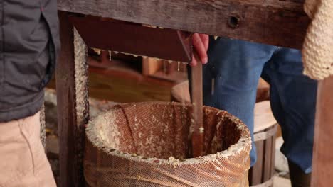 Jemand-Gibt-Äpfel-In-Den-Trichter-Der-Apfelmühle,-Während-Ein-Anderer-Den-Brei-Im-Maschenfass-Umrührt