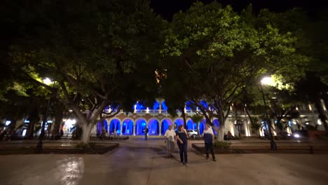 Pushing-in-to-the-Municipal-building-at-dusk-with-its-blue-lights-next-to-the-plaza-grande-in-Merida,-Mexico