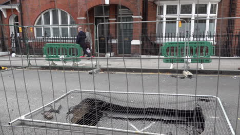 UK-February-2019---People-walk-past-a-fenced-off-sink-hole-that-has-opened-up-in-the-road-in-London’s-affluent-area-of-Kensington