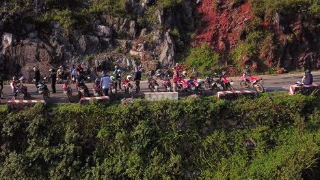 Aerial-side-view-of-a-group-of-motorcyclists-resting-on-the-side-of-the-road,-along-the-Ma-Pi-Leng-Pass-in-the-late-afternoon