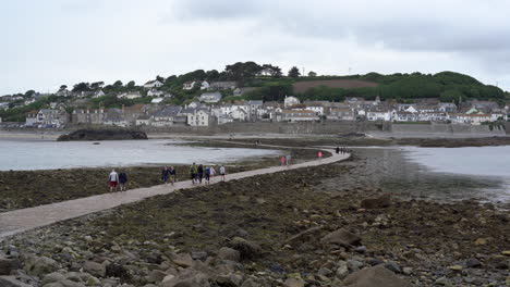 Turistas-Caminando-Por-La-Calzada-Que-Conduce-A-Marazion-Desde-El-Castillo-Medieval-Inglés-Y-La-Iglesia-Del-Monte-De-San-Miguel-En-Cornualles-En-Un-Día-Nublado-De-Primavera,-Alejar-Imágenes-De-4k