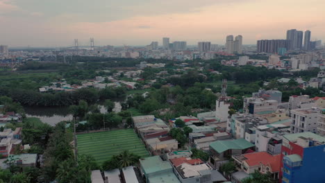 Evening-Flight-over-Medium-density-and-low-density-housing,-a-soccer-field-and-wetlands-towards-Phu-My-Bridge-d7-HCMC