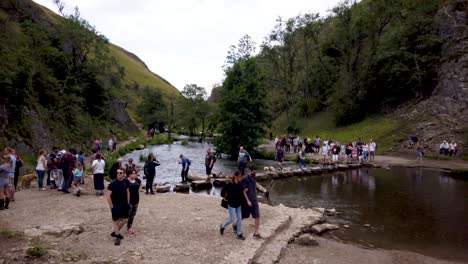 Dovedale-Stepping-Stones-En-Derbyshire,-Peak-District,-Inglaterra,-Reino-Unido-Mostrando-Multitudes-De-Turistas-Cruzando-Los-Stepping-Stones-Sobre-El-Río-Dove