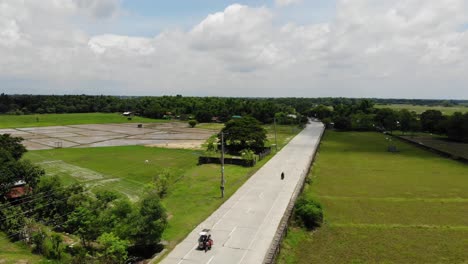 Toma-Aérea-De-Una-Carretera-De-Dos-Carriles-Con-Tráfico-Mínimo-En-La-Provincia-De-Malasiqui,-Pangasinan,-Filipinas,-Rodeada-De-Enormes-Campos-Agrícolas