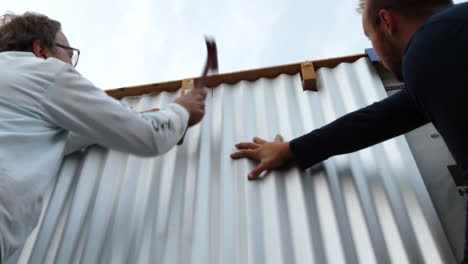 A-crew-of-construction-workers-hammering-and-installing-industrial-metal-siding-on-a-tiny-house-job-site