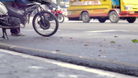 Parked-scooter-detail-in-the-foreground-as-traffic-goes-by-in-the-background,-busses-cars-on-the-road