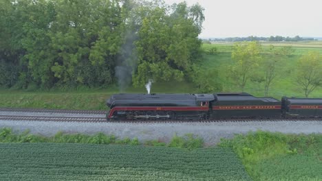 Una-Vista-Aérea-De-Un-Tren-De-Vapor-No-611-Que-Sopla-Humo-A-Través-Del-Campo-Agrícola-En-Un-Día-Soleado-De-Verano-Con-Campos-Verdes