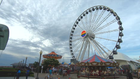 Editorial,-established-shot,-view-of-Navy-Pier-Chicago,-Ferris-Wheel-rotating,-carousel-,-rides-,-people-passing-enjoying-summer-time,-Beautiful-sky-and-clouds