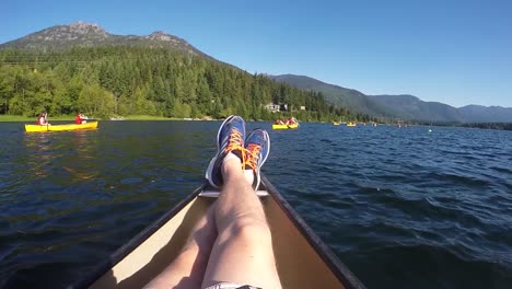 Punto-De-Vista-De-Cámara-Lenta-Filmado-Como-Un-Hombre-Descansando-Las-Piernas-En-Un-Bote,-Gente-En-Canoa-En-Un-Lago