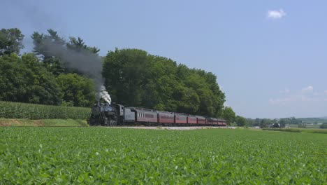 Una-Máquina-De-Vapor-De-1924-Con-Un-Tren-De-Pasajeros-Que-Echa-Humo-Y-Viaja-A-Lo-Largo-De-La-Campiña-Amish-En-Un-Día-De-Verano