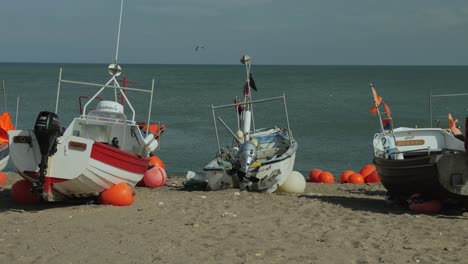 Fisherman-boats-with-waving-flags-at-the-beach-with-water-in-background,-medium-panning-shot