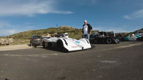 Hombre-Hablando-Con-El-Corredor-Sentado-En-Su-Auto-De-Carreras-Blanco-Con-Casco-En-La-Colina-En-Imtahleb-Malta--Gopro-Tilt-Pan-Shot