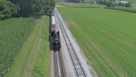 Aerial-View-of-a-1910-Steam-Engine-with-Passenger-Train-Puffing-Smoke-Traveling-Along-the-Amish-Countryside-on-a-Sunny-Summer-Day-as-Seen-by-a-Drone