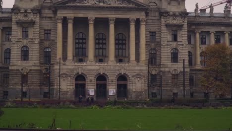 Césped-Exuberante-Y-Gente-Caminando-Frente-Al-Museo-Histórico-De-Etnografía-En-Budapest,-Hungría,-Con-Grúa-Torre-Erigida-En-La-Parte-Trasera---Tiro-Panorámico