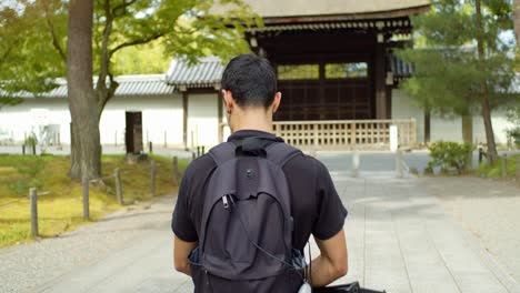 Person-walking-towards-a-wooden-gate-entrance-surrounded-by-trees-in-the-background-in-Kyoto,-Japan-soft-lighting-4K