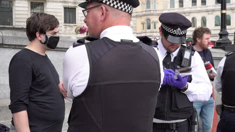 Un-Oficial-De-Policía-Toma-Notas-Durante-Una-Parada-Y-Registro-De-Activistas-Ambientales-Enmascarados-Que-Asisten-A-Una-Protesta-Del-Partido-Más-Allá-De-La-Política-En-Trafalgar-Square