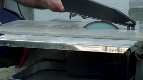 Side-view-of-man-cutting-ceramic-tiles-on-small-tile-cutting-machine-with-water-culling