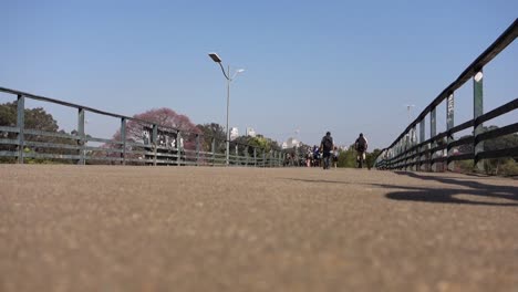 Vista-Trasera-Del-Hombre-Caminando-En-El-Paso-Elevado-Y-Ciclista-Cruzándolo-A-Gran-Velocidad