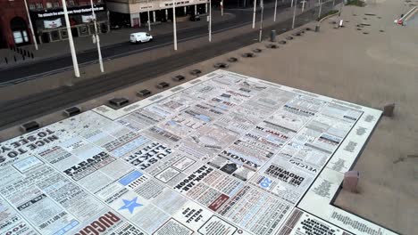 Blackpool-comedy-carpet-comedian-jokes-promenade-floor-aerial-view-descending-tilt-up-to-seaside-street