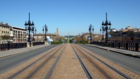 Bikers-crossing-Pont-de-Pierre-bridge-over-Garonne-river-during-the-COVID-19-pandemic,-Walking-stabilized-center-shot-over-tram-tracks