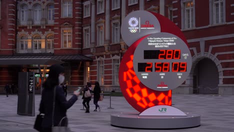 Countdown-Uhr-Für-Die-Olympischen-Spiele-In-Tokio-Mit-Pendlern-Mit-Gesichtsmasken,-Die-Während-Der-Koronakrise-2020-Durch-Den-Rahmen-Fahren