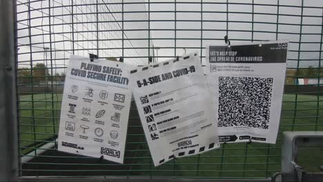 Covid-Sicherheitsschilder-Zusammen-Mit-Der-Kontakt-Track-and-Trace-QR-Code-App-Hängen-Am-Zaun-Bei-Goals-Ruislip