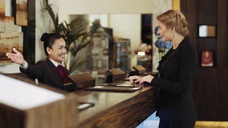 Recepcionista-Femenina-En-Un-Hotel-Asiático-Entregando-La-Llave-De-La-Puerta-De-Una-Habitación-De-Hotel-A-Una-Mujer-De-Negocios---Tiro-Medio,-Cámara-Lenta