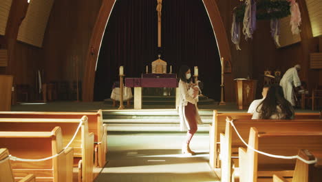 Pasillo-De-Una-Iglesia-Católica-Con-Madre-Enmascarada-Que-Lleva-A-Un-Bebé-Durante-La-Pandemia-Del-Coronavirus-Covid-19-En-Cámara-Lenta