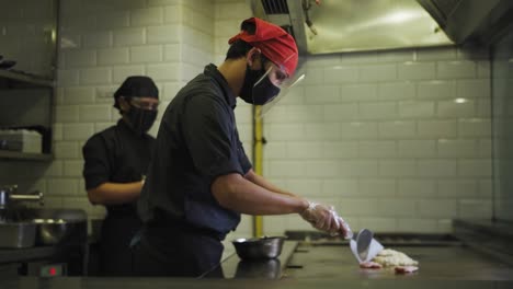 Chef-In-Face-Mask-And-Face-Shield-Cooking-Okonomiyaki-On-Griddle-In-Restaurant