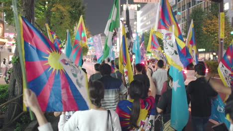 View-Behind-Group-Of-Uyghur-And-Tibetan-Protesters-Marching-In-The-Street-With-Flags