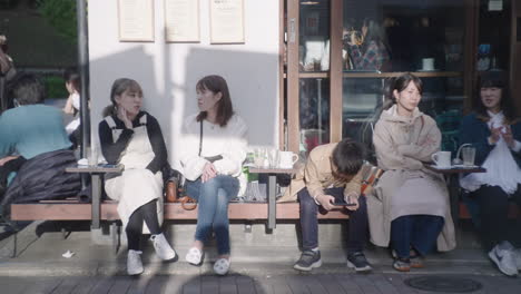 Japanese-People-Chatting,-Drinking-Coffee-While-Sitting-Outside-A-Cafe-On-A-Sunny-Day-In-Tokyo,-Japan