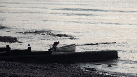 Ein-Fischer-Schiebt-Sein-Boot-Aufs-Meer-Hinaus-Und-Rudert-Mit-Rudern-über-Kleine-Wellen,-Die-Im-Morgengrauen-An-Die-Küste-Rollen