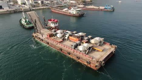 Barge-loaded-with-Concrete-mixer-trucks-pulled-to-port-by-a-Tugboat-in-Hong-Kong-bay,-Aerial-view