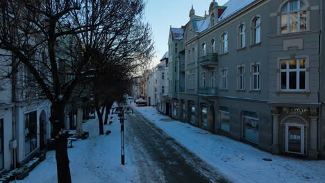 El-Dron-Despega-De-La-Calle-Cubierta-De-Nieve-Del-Antiguo-Distrito-De-La-Ciudad-De-Sopot-Al-Atardecer-Muestra-Fachadas-De-Edificios-Antiguos