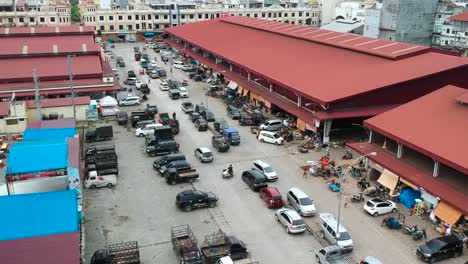 Imágenes-Aéreas-De-La-Tienda-Local-Del-Mercado-De-Alimentos-Que-Construye-El-Estacionamiento-De-Automóviles-Y-Camiones-Y-La-Gente-Camina-Para-Comprar-Frutas-Y-Verduras-Frescas-Temprano-En-La-Mañana