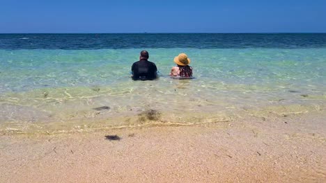 Pareja-Sentada-Junto-A-Las-Olas-Del-Océano-Pasando-Suavemente-Cerca-De-La-Playa