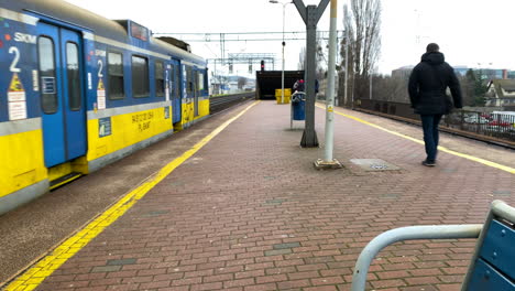 People-Walking-On-Brick-Pavement-Sidewalk-With-Rustic-Train-Traveling-During-Winter-Daytime