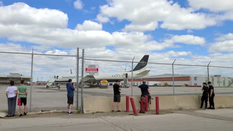 Fotógrafos-Y-Espectadores-Fuera-De-La-Valla-Viendo-El-Avión-De-Carga-Dc-8-De-Samaritan&#39;s-Purse-Con-Ucranianos-Repatriados-A-Un-Lugar-Seguro-En-Toronto,-Canadá