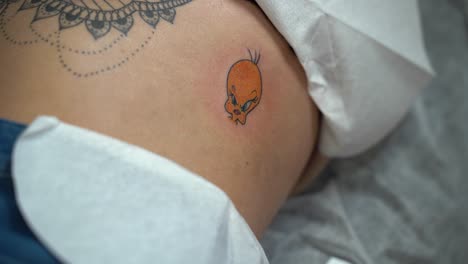 The-tattoo-artist-is-tattooing-Tweety-canary-from-Looney-tunes-on-a-woman's-skin