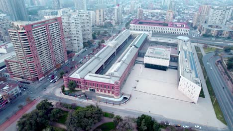 Aerial-orbit-of-Bicentennial-Army-complex-structure-and-square-surrounded-by-Santiago-Centro-neighborhood-buildings,-Chile